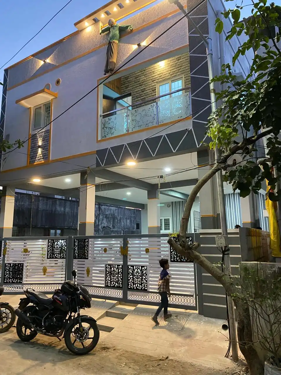 Completed G+2 residence in Vinayagapuram at dusk, with lit balconies, a geometric façade band and a decorative front gate