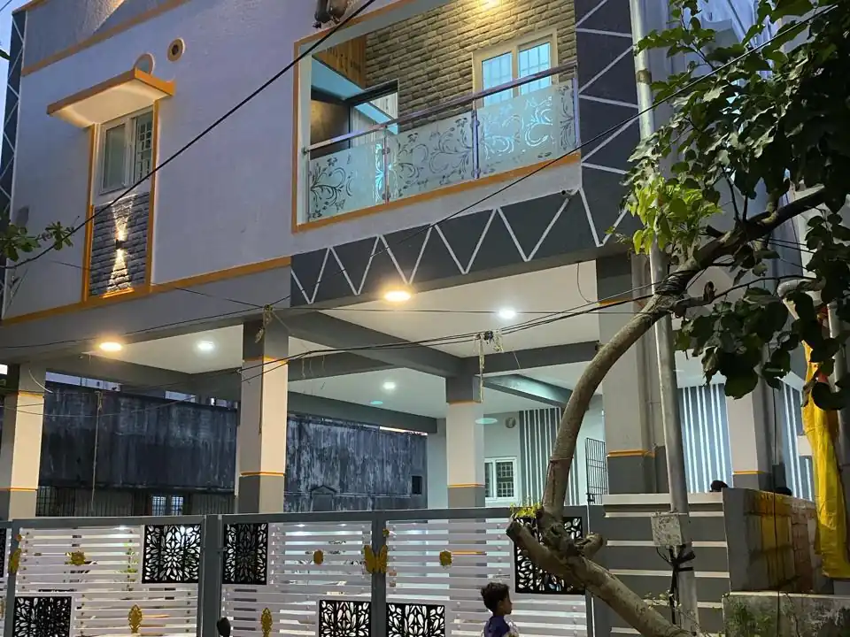 Completed G+2 residence in Vinayagapuram at dusk, with lit balconies, a geometric façade band and a decorative front gate